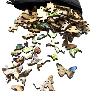 May include: A black drawstring bag spills out wooden jigsaw puzzle pieces. Many pieces are butterfly-shaped, with natural wood grain and colorful imagery. The puzzle pieces are scattered, suggesting a completed puzzle or a work in progress.