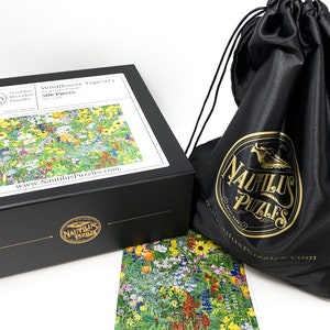 May include: A black box set of a 506-piece jigsaw puzzle titled "Wildflower Tapestry" by Nautilus Puzzles. The puzzle image shows a colorful field of wildflowers. A black drawstring bag with the Nautilus Puzzles logo is also included.