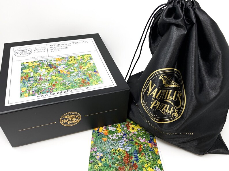 May include: A black box set of a 506-piece jigsaw puzzle titled "Wildflower Tapestry" by Nautilus Puzzles. The puzzle image shows a colorful field of wildflowers. A black drawstring bag with the Nautilus Puzzles logo is also included.