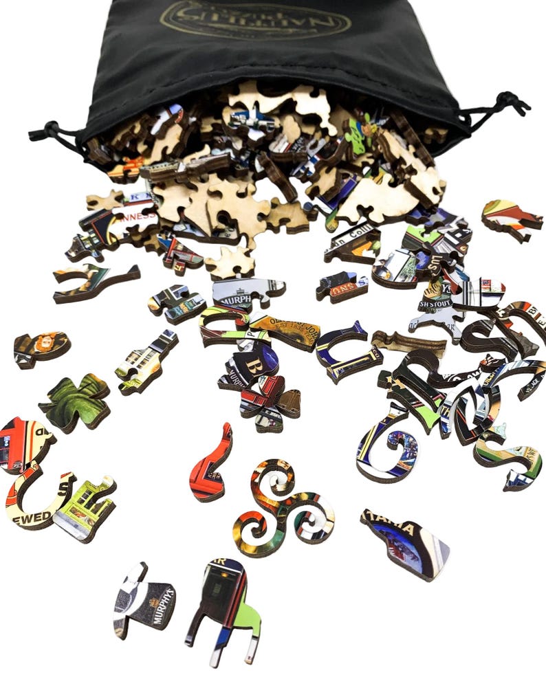 May include: A black drawstring bag spills out wooden puzzle pieces. The pieces are various shapes and sizes, with colorful images and text. The puzzle pieces are scattered on a white surface, creating a visually engaging display.