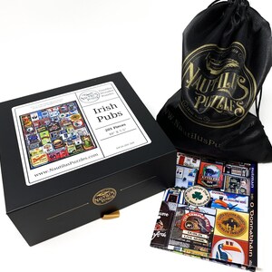 May include: A black box set featuring a 201-piece jigsaw puzzle with an Irish Pubs theme. The box has a gold-colored clasp and a white label with the puzzle's details. A black drawstring bag with a gold logo and a completed puzzle image are also visible.