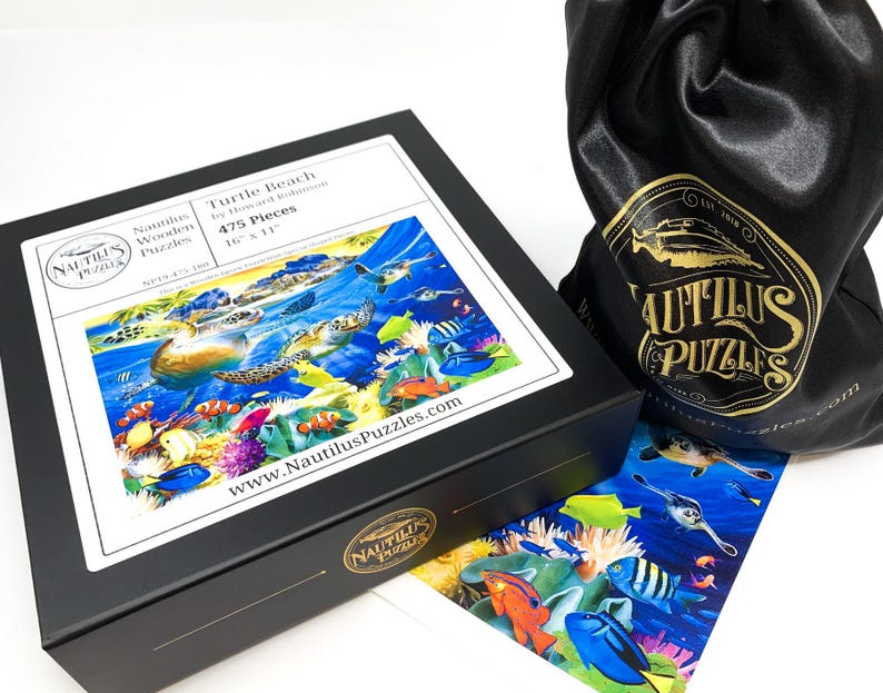 May include: A black box with a puzzle titled "Turtle Beach" by Howard Robinson. The puzzle is 16" x 11" and features an underwater scene with sea turtles and colorful fish. A black drawstring bag with a gold logo is next to the box.