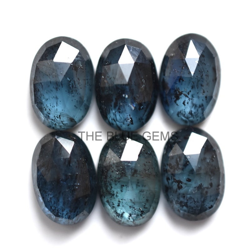 May include: Six faceted oval blue gemstones with a dark blue color and a cloudy appearance.