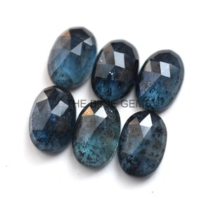 May include: Six faceted oval blue gemstones with a dark blue and black marbled pattern. The gemstones are arranged in a cluster on a white background.