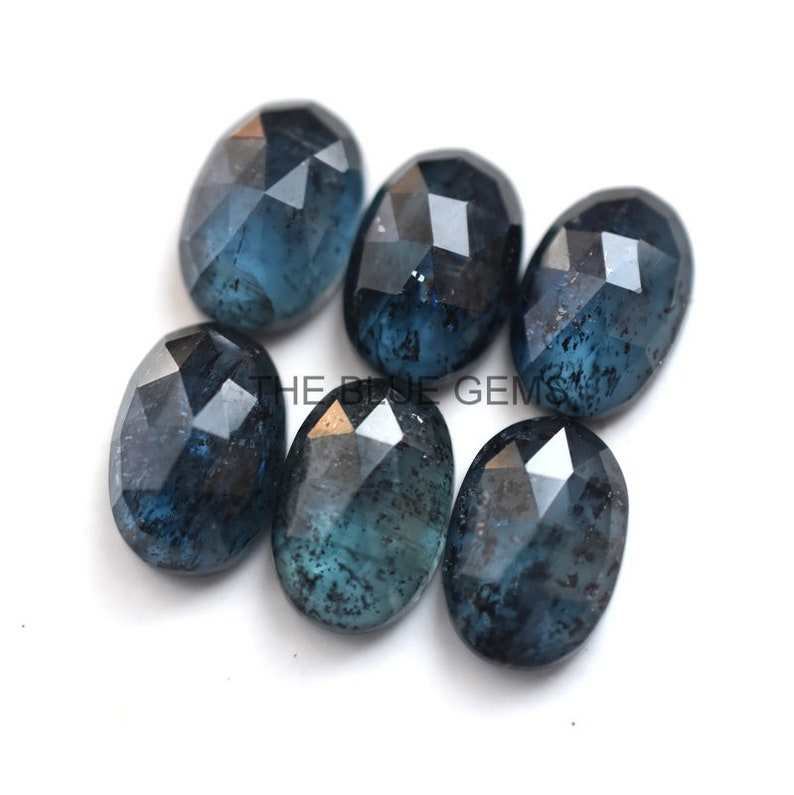 May include: Six faceted oval blue gemstones with a dark blue and black marbled pattern. The gemstones are arranged in a cluster on a white background.