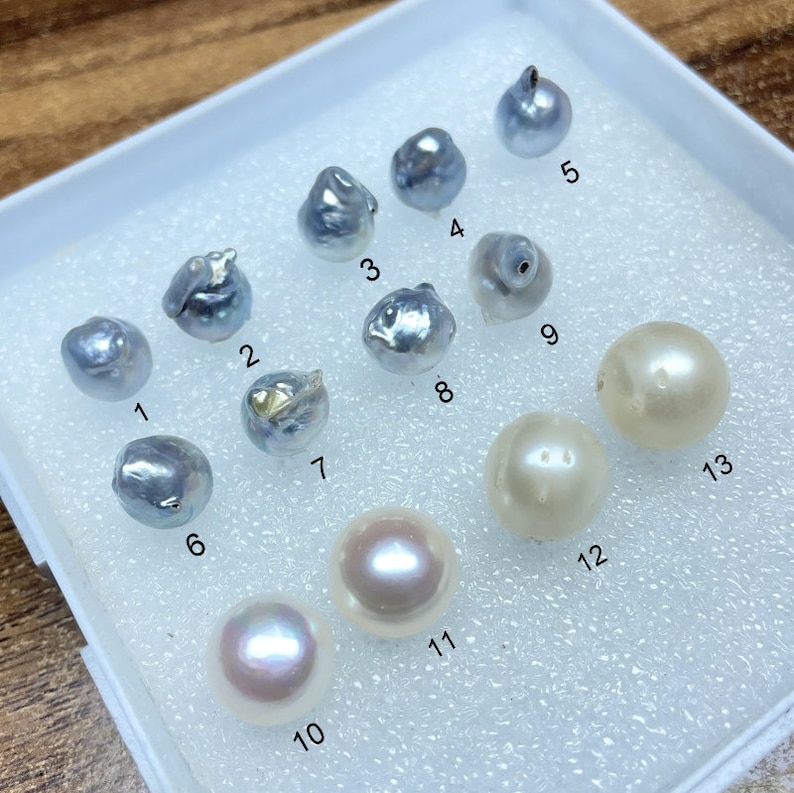 Puede incluir: Una colecci&oacute;n de 13 perlas en una bandeja blanca. Las perlas son de varios tonos de blanco, gris y azul. Las perlas est&aacute;n numeradas del 1 al 13.