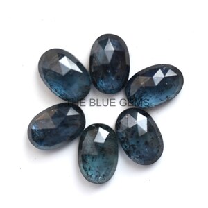 May include: Six oval-shaped, faceted, dark blue gemstones with a cloudy, translucent appearance. The gemstones are arranged in a circle on a white background.