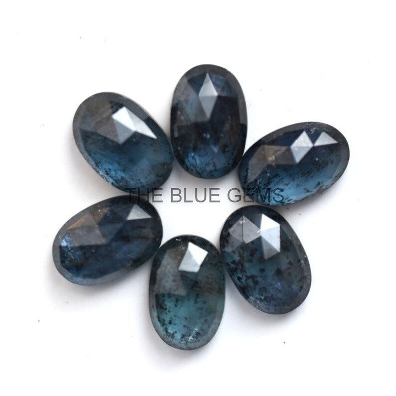 May include: Six oval-shaped, faceted, dark blue gemstones with a cloudy, translucent appearance. The gemstones are arranged in a circle on a white background.
