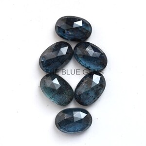 May include: Six dark blue faceted oval gemstones. The gemstones are arranged in a cluster on a white background.