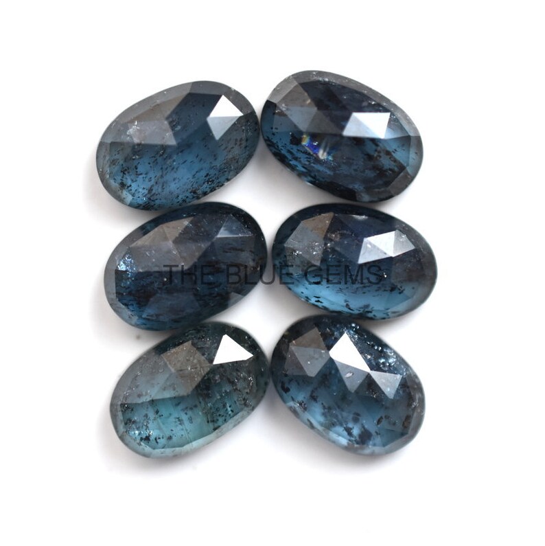 May include: Six oval-shaped blue gemstones with a faceted cut. The gemstones have a dark blue color with a slight shimmer.