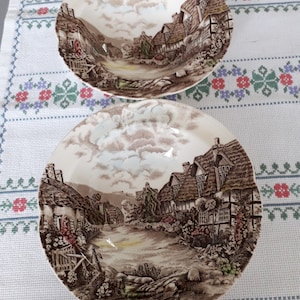 Puede incluir: Dos cuencos de cerámica marrón y blanco con un diseño de escena de cabaña. Los cuencos tienen un borde festoneado y un esmalte marrón y blanco.