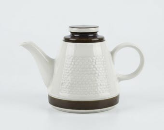Peut inclure: Une théière en céramique avec un corps de couleur crème et un motif en nid d'abeille texturé sur les côtés. La théière comprend un couvercle marron foncé, une bande marron foncé assortie à la base, un bec verseur et une anse arrondie.