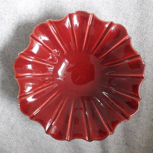 Peut inclure: Un bol en céramique rouge avec un bord festonné et un motif cannelé. Le bol est verni et a une finition brillante.