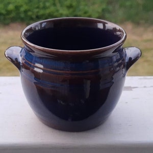Può includere: Un piccolo vaso in ceramica blu scuro con accenti marroni e due manici. Il vaso è smaltato e ha una finitura liscia.