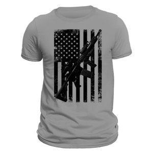 May include: A grey t-shirt with a distressed American flag design featuring a black silhouette of a rifle.