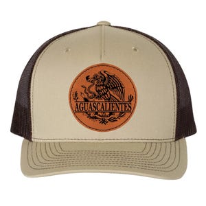 May include: A tan and brown trucker hat featuring a circular patch with the word "AGUASCALIENTES" and an eagle emblem. The hat has a mesh back and a curved brim.