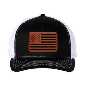 May include: A black and white trucker hat with a brown leather American flag patch on the front.