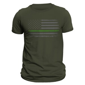 May include: A green, gray, and white distressed American flag with a thin green line across the middle. The flag is printed on a dark green t-shirt.