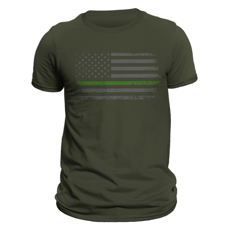 May include: A green, gray, and white distressed American flag with a thin green line across the middle. The flag is printed on a dark green t-shirt.