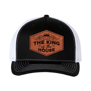 May include: Black and white trucker hat with a brown leather patch that says "THE KING of the HOUSE" with a crown above the text.