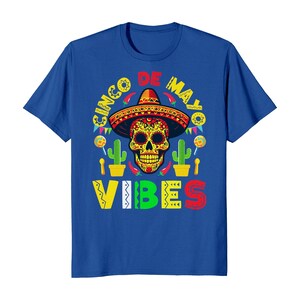 May include: Blue t-shirt with a colourful Cinco de Mayo design featuring a sugar skull wearing a sombrero, cacti, and the text "Cinco de Mayo Vibes".