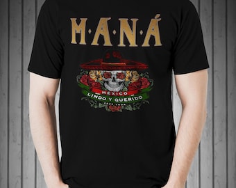Könnte beinhalten: Schwarzes T-Shirt mit einem goldenen "MANA"-Logo und einem Totenkopf, der einen Sombrero trägt, umgeben von roten Rosen. Der Text "MEXICO LINDO Y QUERIDO 2023 TOUR" befindet sich unter dem Totenkopf.