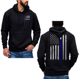 May include: Black hooded sweatshirt with a thin blue line American flag on the left chest and a full-size American flag with a thin blue line on the back. The text "LAST NAME" is printed vertically on the back flag.