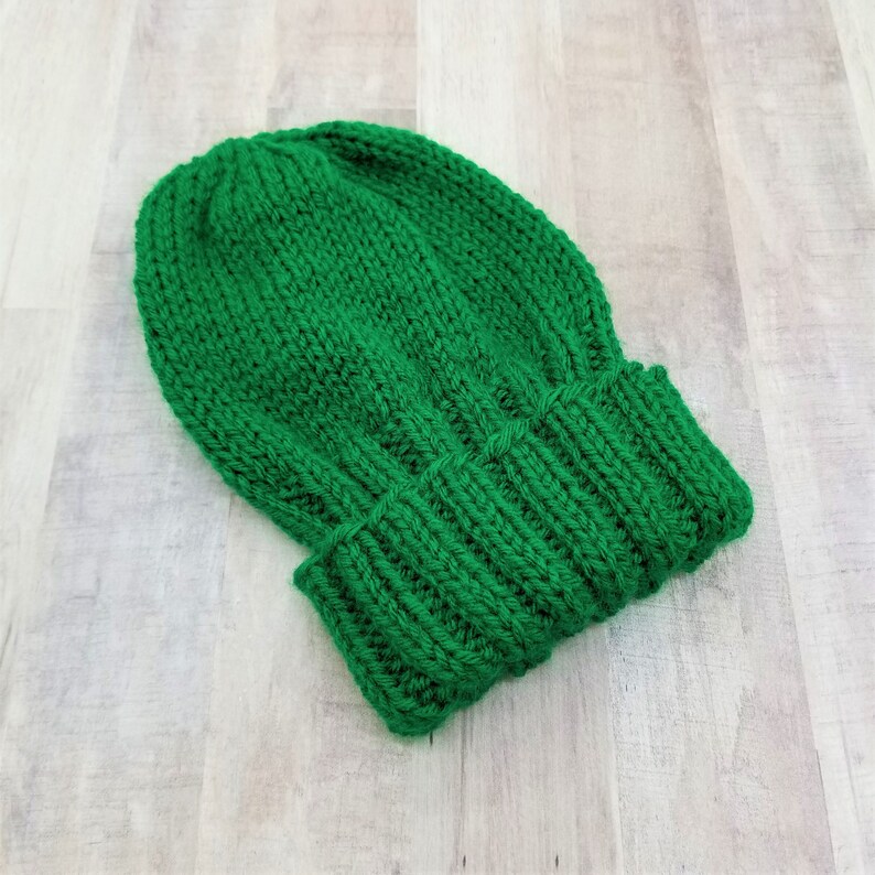 May include: A solid green knitted beanie hat. The hat is made of a soft, thick yarn and has a simple, classic design.