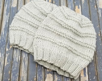 May include: Two knitted hats in a light gray color. The hats are made with a ribbed stitch pattern.