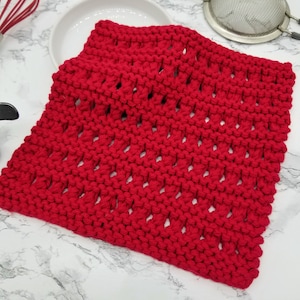 May include: Red knitted dishcloth with a diamond pattern. The dishcloth is made of cotton yarn and has a textured surface.