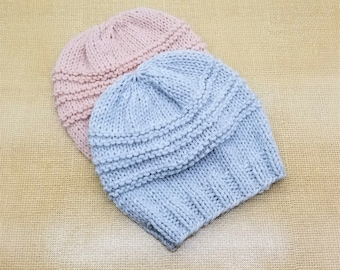 May include: Two knitted hats, one light blue and one light pink, are shown on a brown burlap background.