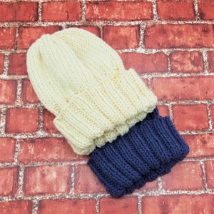 May include: A white knitted beanie with a blue knitted cuff. The beanie is folded over and the cuff is visible.