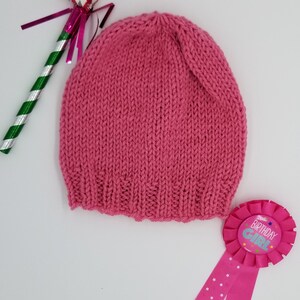 May include: A pink knitted hat with a birthday girl ribbon and a party favor.