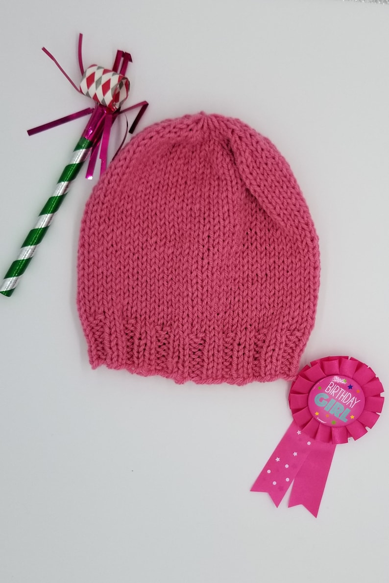 May include: A pink knitted hat with a birthday girl ribbon and a party favor.