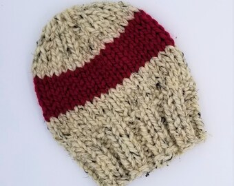 May include: A beige knitted beanie with a wide red stripe across the front.