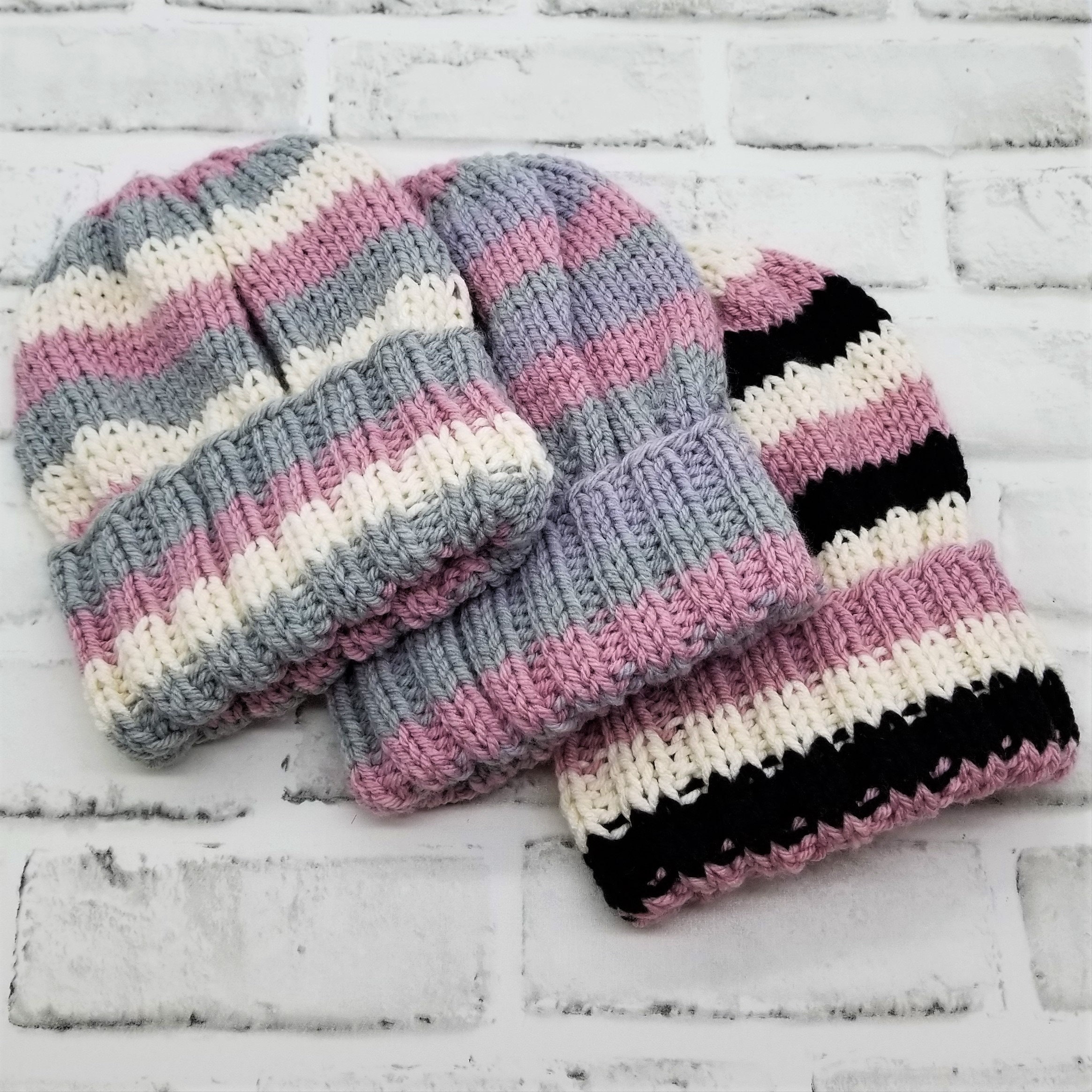 May include: Three striped knit hats in pink, gray, and white. One hat has black stripes.
