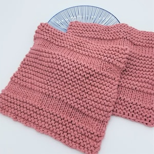 May include: Two pink knitted dishcloths, made with a simple stitch pattern, are stacked on top of each other. The dishcloths are made of a soft, absorbent material and are perfect for cleaning up spills and messes in the kitchen.