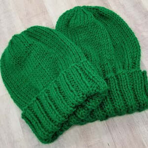 May include: Two green knitted beanies, one on top of the other.