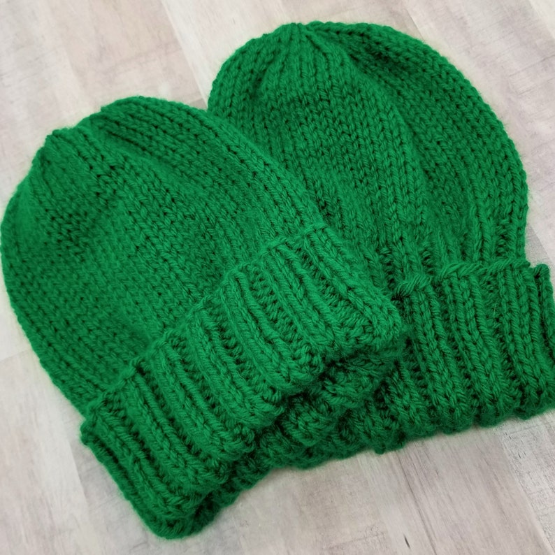 May include: Two green knitted beanies, one on top of the other.