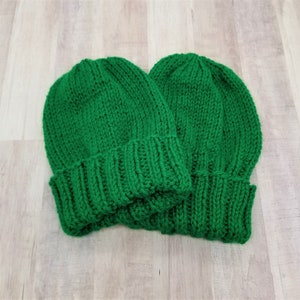 May include: Two green knitted beanies, one on top of the other.