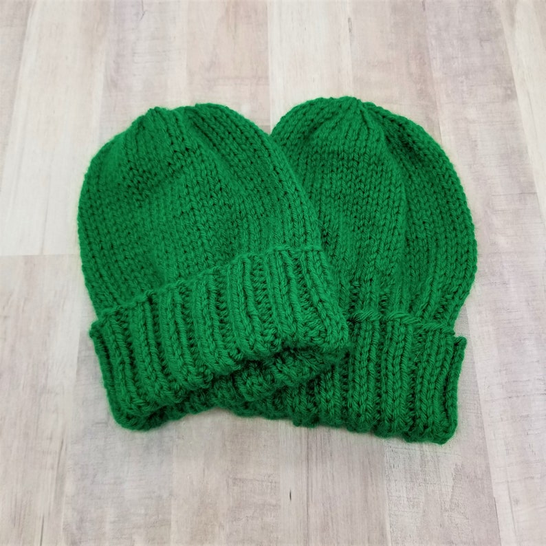 May include: Two green knitted beanies, one on top of the other.