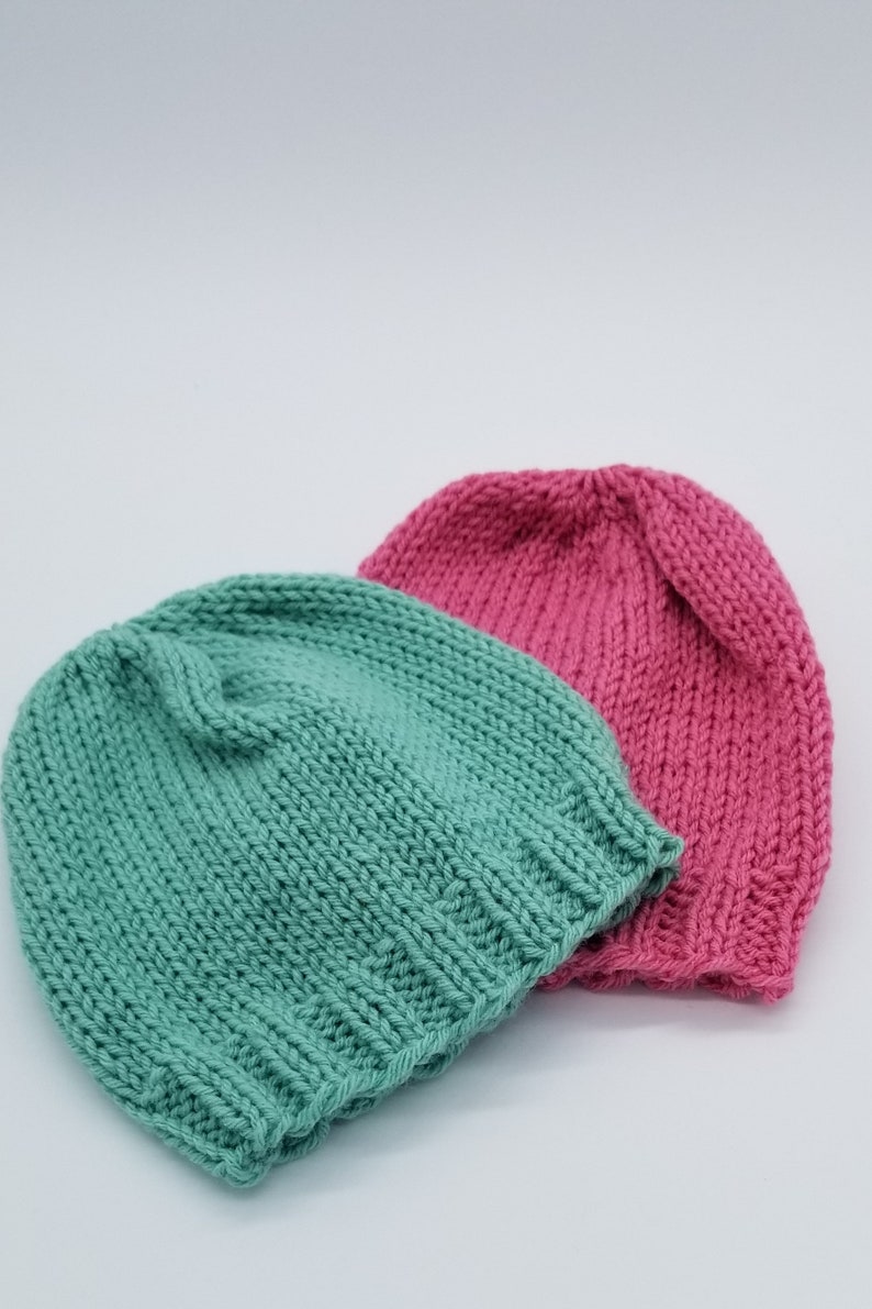 May include: Two knitted hats, one teal green and one pink. The hats are made of soft yarn and have a simple, classic design.