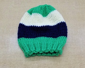 May include: A green, white, and navy blue striped knitted hat. The hat has a ribbed texture and a folded brim.