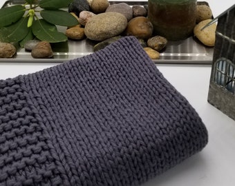 May include: A soft, grey knitted throw blanket with a textured pattern. The blanket is folded and placed on a white surface.