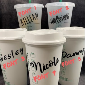 Pode incluir: Cinco copos de caf&eacute; reutiliz&aacute;veis brancos com texto preto. Os copos s&atilde;o etiquetados com nomes e estilos de fonte diferentes. Os nomes s&atilde;o Killian, Haleigh, Wesley, Nicole e Danny. Os estilos de fonte s&atilde;o etiquetados como Fonte 1, Fonte 2, Fonte 3, Fonte 4 e Fonte 5.