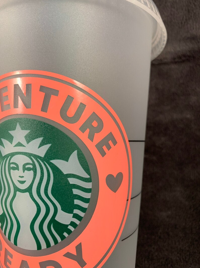 Pode incluir: Uma caneca reutiliz&aacute;vel rosa e cinza com um logotipo da Starbucks e o texto "Adventure Ready" com um cora&ccedil;&atilde;o.