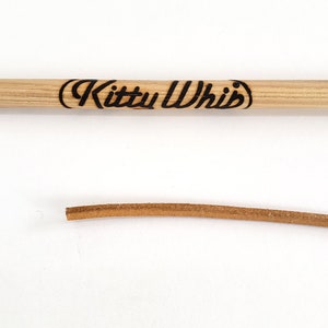 The trademark brand on the handle and the  end of the leather cord of the KittyWhip Leather® wand cat toy displayed against a white background.