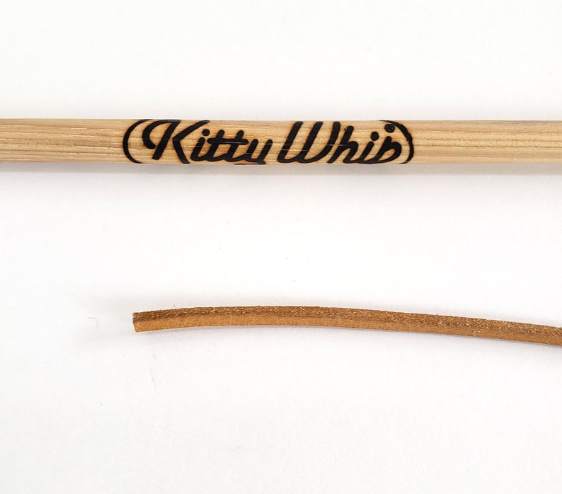 The trademark brand on the handle and the  end of the leather cord of the KittyWhip Leather® wand cat toy displayed against a white background.