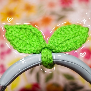 May include: Green crocheted leaf-shaped headphone covers. The covers are attached to the headband of a pair of gray headphones.