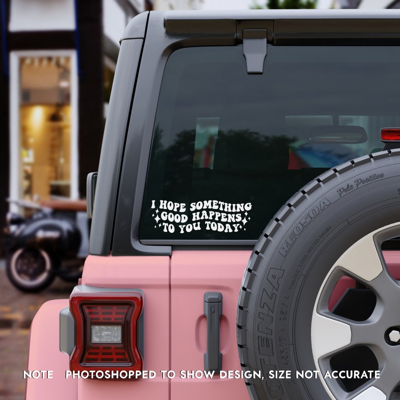 May include: A white vinyl decal applied to the rear window of a pink vehicle. The decal features the text I HOPE SOMETHING GOOD HAPPENS TO YOU TODAY in a bold, retro-style font, accented by small four-pointed star shapes surrounding the lettering.